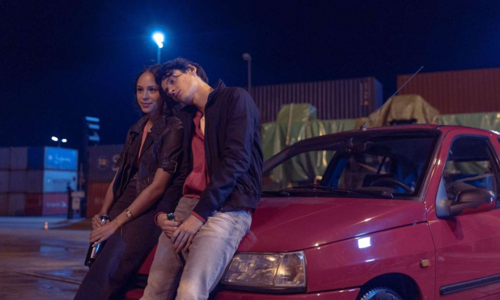 Yusuf Arslan et une jeune femme assis sur une voiture rouge la nuit dans la série Banksters sur HBO Max