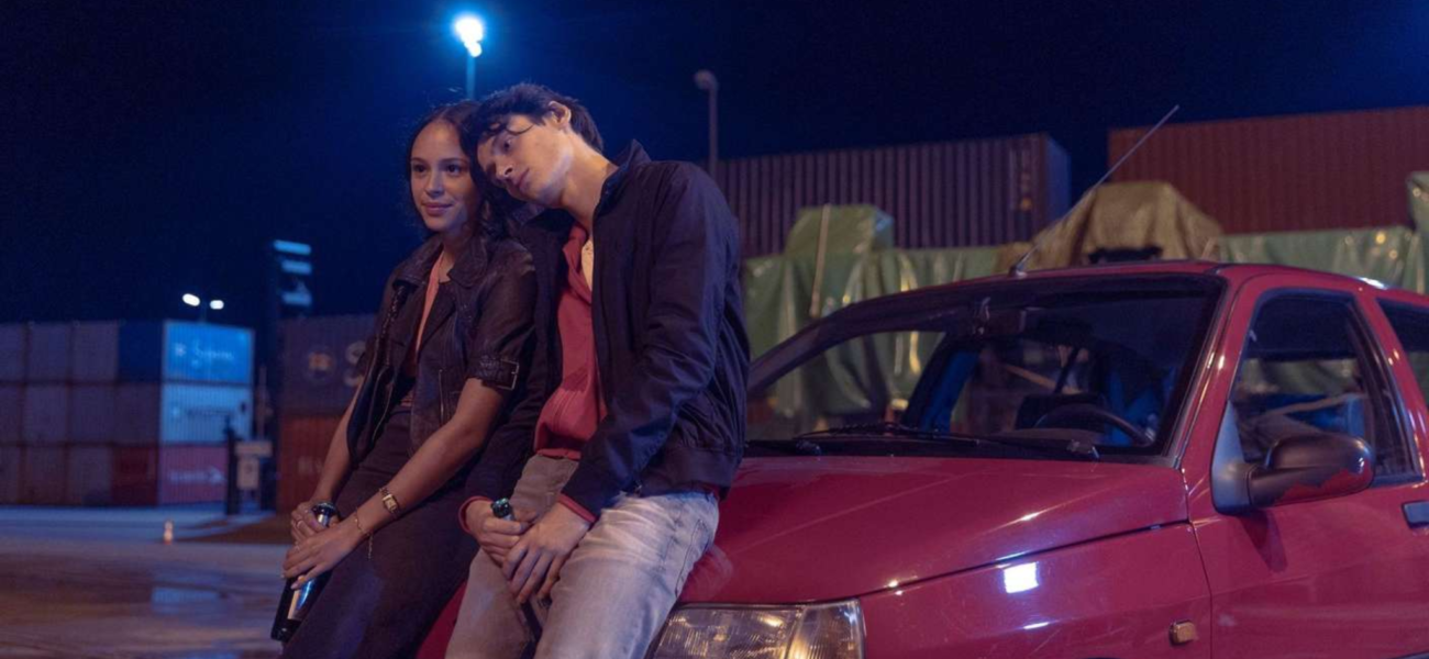 Yusuf Arslan et une jeune femme assis sur une voiture rouge la nuit dans la série Banksters sur HBO Max