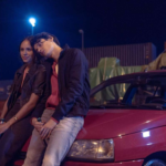 Yusuf Arslan et une jeune femme assis sur une voiture rouge la nuit dans la série Banksters sur HBO Max