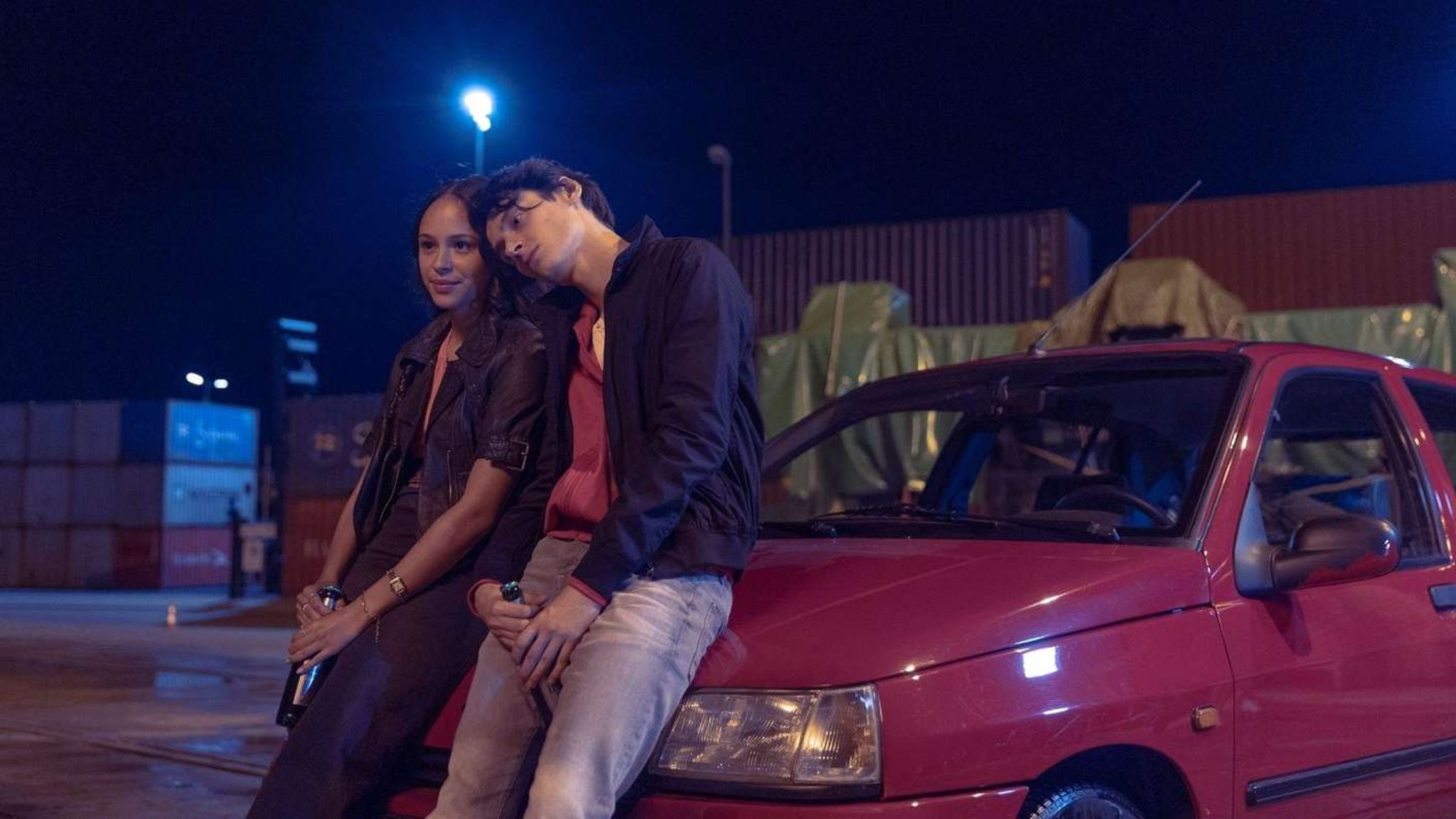 Yusuf Arslan et une jeune femme assis sur une voiture rouge la nuit dans la série Banksters sur HBO Max