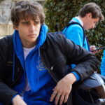 James assis sur une moto devant une école internationale à Milan dans Love Me Love Me sur Prime Video