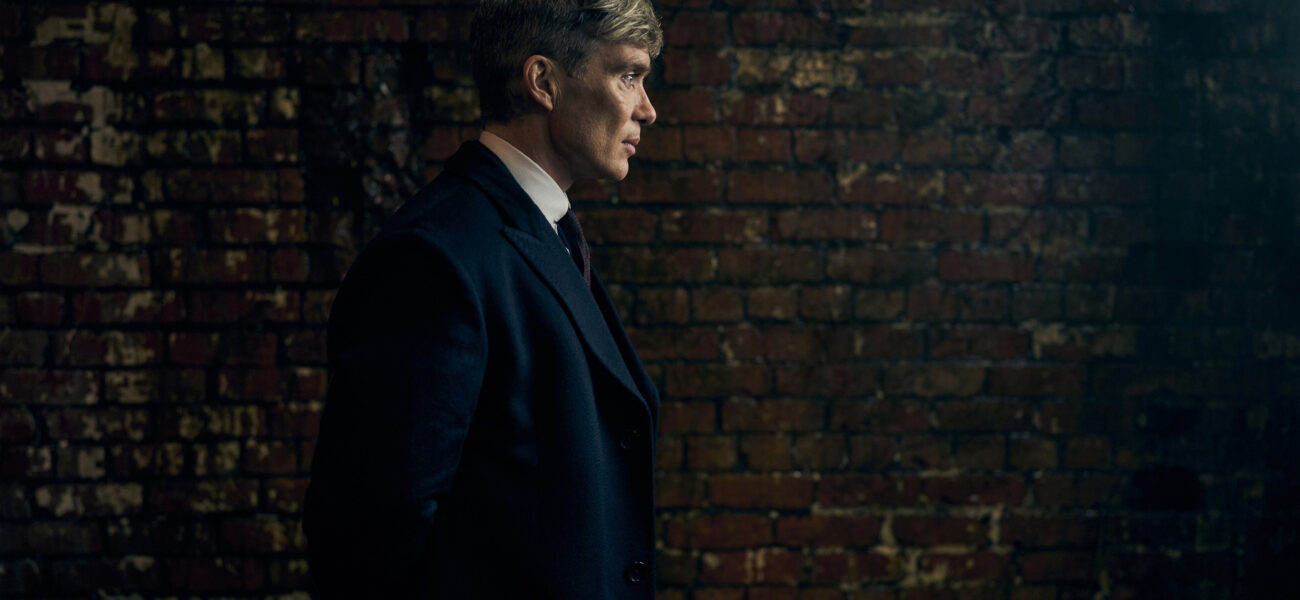 Tommy Shelby en costume sombre devant un mur de briques dans Peaky Blinders
