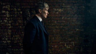 Tommy Shelby en costume sombre devant un mur de briques dans Peaky Blinders