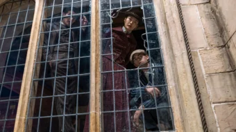 Scène de la série Young Sherlock montrant de jeunes personnages observant Oxford depuis une fenêtre grillagée.