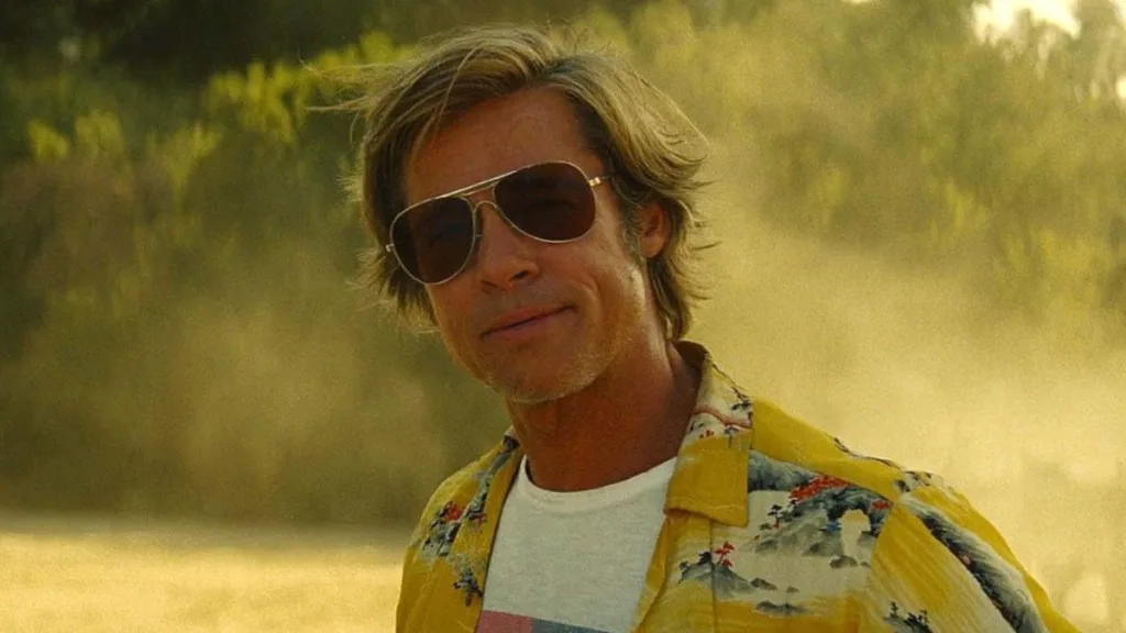 Cliff Booth, incarné par Brad Pitt, portant des lunettes de soleil et une chemise jaune, dans une scène ensoleillée de Once Upon a Time in Hollywood.